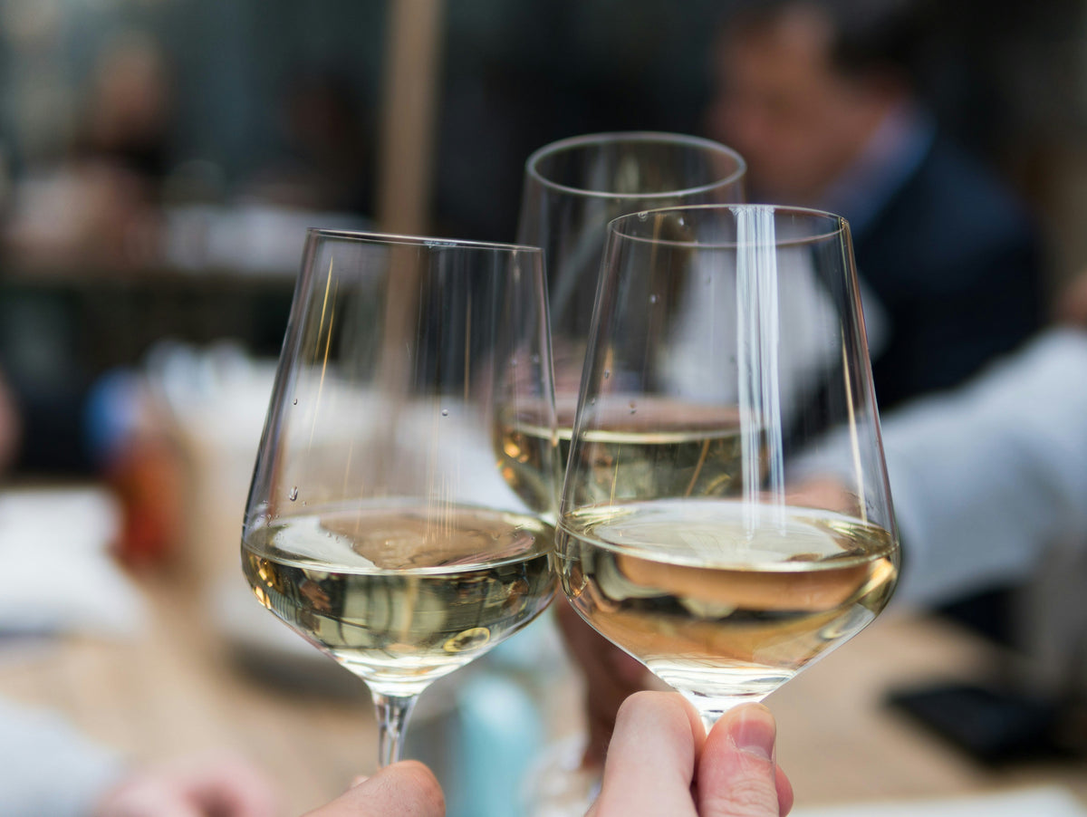 Three glasses of white wines being chinked at a tasting table