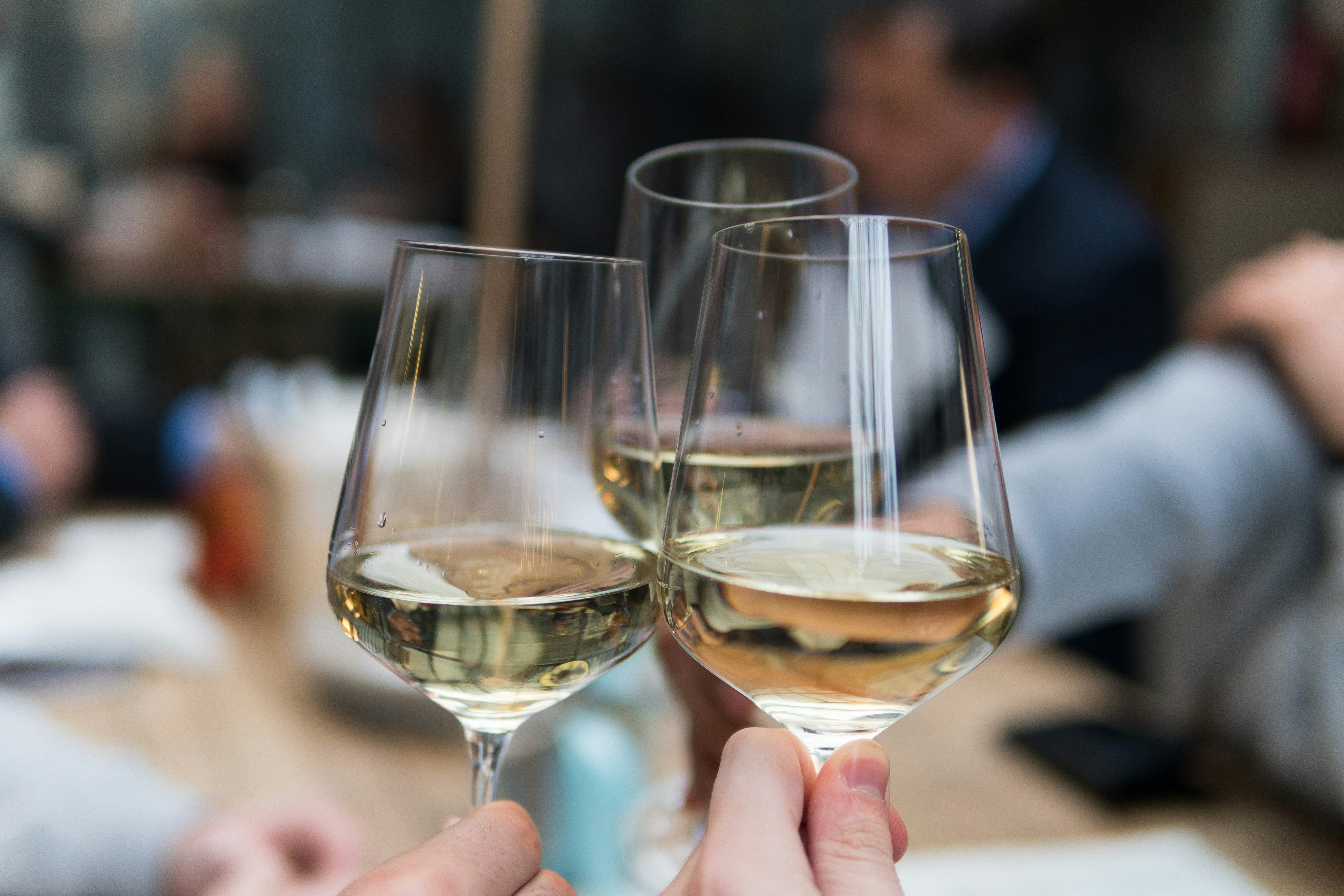 Three glasses of white wines being chinked at a tasting table