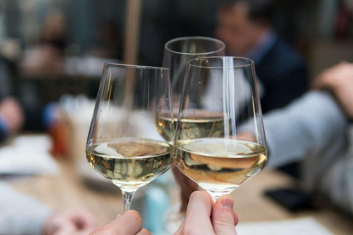 Three glasses of white wines being chinked at a tasting table